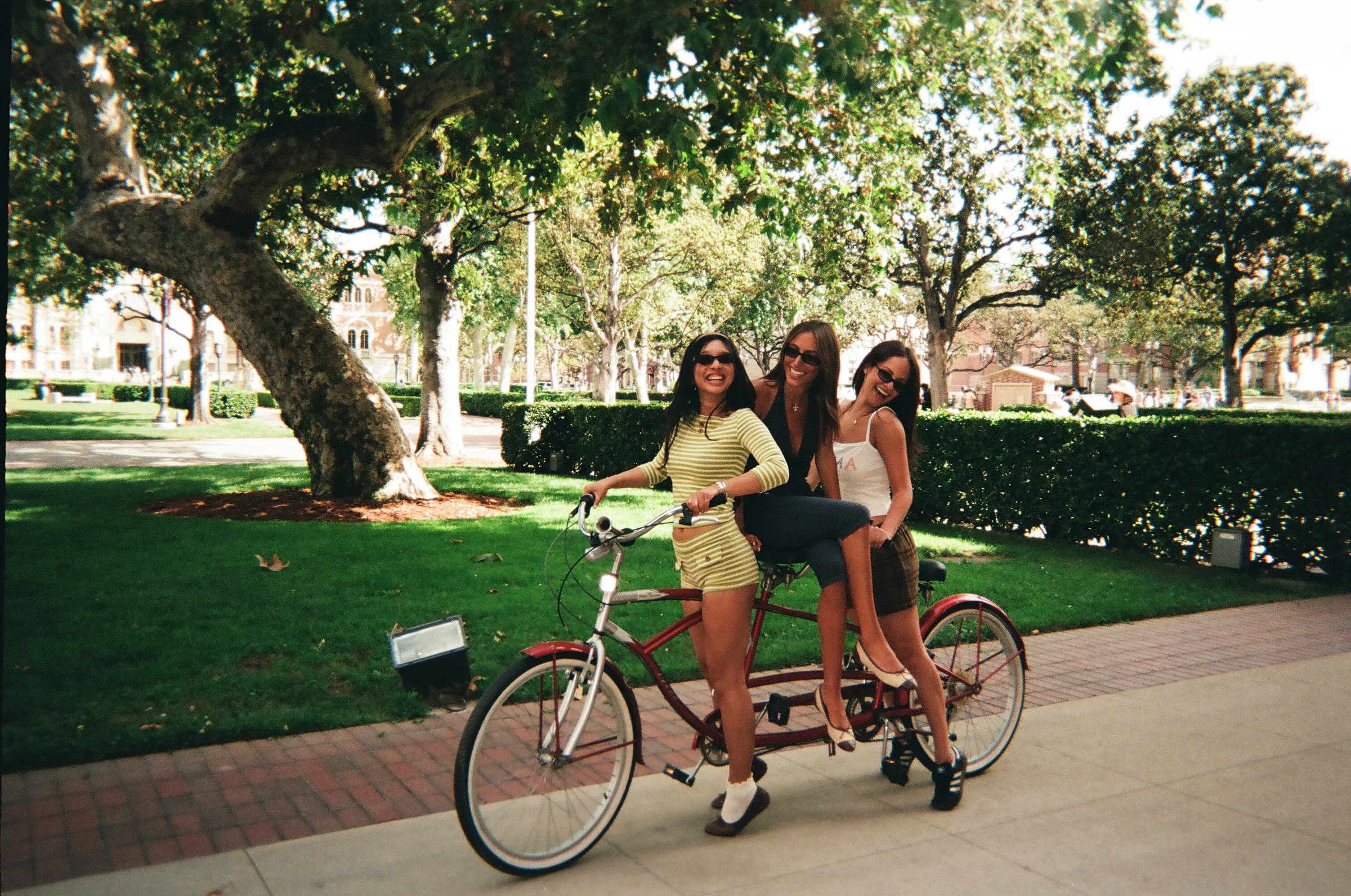 Three models riding a tandem bike across campus